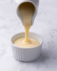 Pouring condensed milk in a bowl over marble background