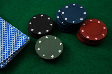 Stacks of poker chips in various colors are neatly arranged on a green felt table beside a blue deck of playing cards, suggesting a fun evening of card games.