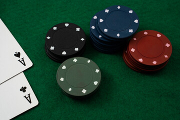 Colorful poker chips in various stacks are positioned alongside two playing cards showing aces, set on a green felt surface under soft lighting, indicating a casual game night atmosphere.
