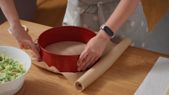 Preparing a baking pan for a recipe. A woman lines a springform cake tin with non-stick parchment paper. The process of getting bakeware ready for a homemade pie, cake, or quiche.