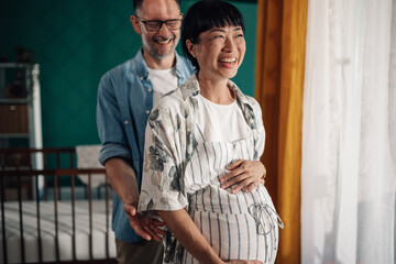 Fototapeta premium Happy pregnant woman holding belly with husband in nursery