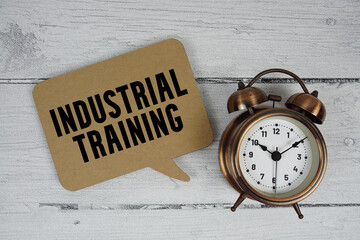 Industrial training text with alarm clock on wooden background