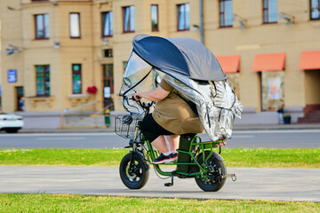Woman riding modern electric tricycle with protective canopy cover on street, sustainable transport, urban commuting lifestyle convenience. Female rider on electric pedal powered tricycle in motion