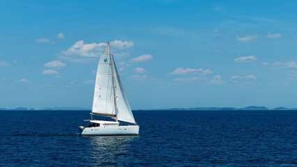 Obraz premium Sailing catamaran with open sails. Sailing catamaran in the middle of the sea in a tropical landscape. Sailing boat with open sails