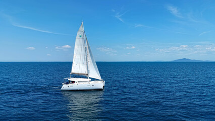Fototapeta premium Sailing catamaran with open sails. Sailing catamaran in the middle of the sea in a tropical landscape. Sailing boat with open sails