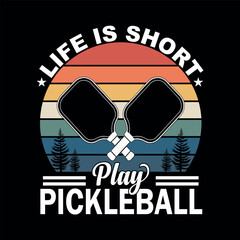 Pickelball Life: A graphic design showcasing a pair of crossed pickleball paddles alongside the optimistic slogan Life is short, play pickleball, perfect for sport