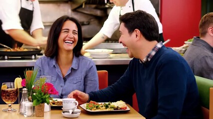 Happy couple laughs while eating lunch in restaurant. Man and woman enjoying casual meal together, symbol of friendship, romance, lifestyle, happiness. Smiling pair shares fun moment at dining table. - Powered by Adobe