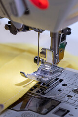 A close-up shot captures the needle of a sewing machine poised above vibrant yellow fabric, ready to create precise stitches. The intricate details of the presser foot and feed dogs are visible.