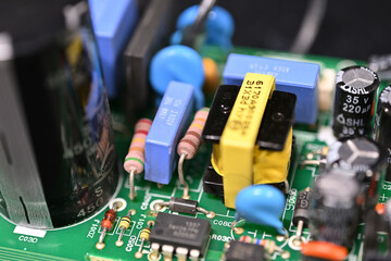 Close-up of various diodes and resistors powered on a printed circuit board next to a capacitor.
