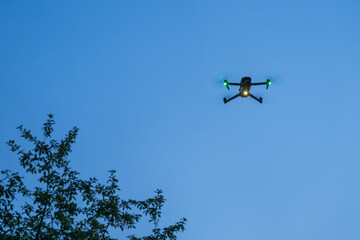 Close-up of a small glowing drone hovering in the evening.
