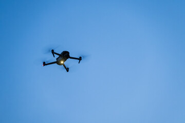 Close-up of a small glowing drone hovering in the evening.
