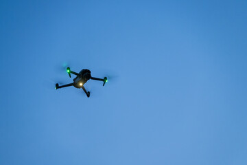Close-up of a small glowing drone hovering in the evening.
