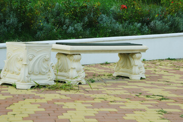 White carved stone bench and urn with spiral elements in the city park. The seat has wooden brown...