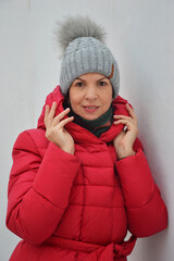 Caucasian woman in red down jacket and gray knitted hat on white background. Women's warm winter clothes.