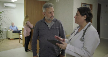 Man expressing relief while speaking with female doctor in clinic hallway, smiling with hand on...