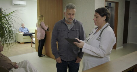 Man expressing relief while speaking with female doctor in clinic hallway, smiling with hand on...