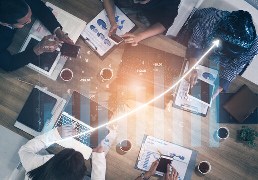 A diverse team collaborates in a meeting environment, analyzing financial data and strategies with laptops and smartphones, fostering innovation. Impute