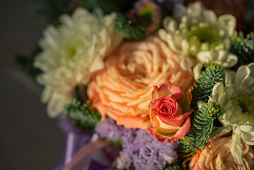 Vibrant bouquet of flowers, featuring a delicate rosebud emerging from a bed of orange roses, white chrysanthemums, and purple lisianthus, creating a beautiful display of color and texture