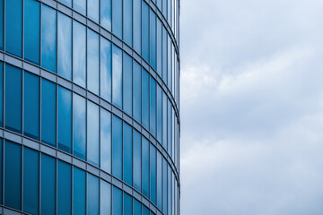 View of skyscraper windows and cloudy sky nearby. Glass walls and cloud background