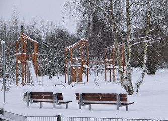 An empty public playground covered in a thick blanket of snow in MÃ¼nster, Germany. Benches and...
