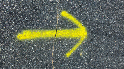 a yellow arrow painted on asphalt, commonly used for temporary ground markings. surveying, land, construction, or infrastructure background. instructional symbol or sign banner.