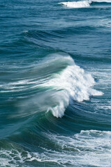 Powerful ocean waves rolling and crashing against the shore create a stunning display of white...