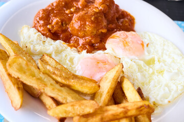 Meatballs in tomato sauce with fried eggs and chips