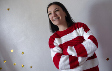 Smiling young woman with braces in a red and white striped sweater stands with arms crossed against...