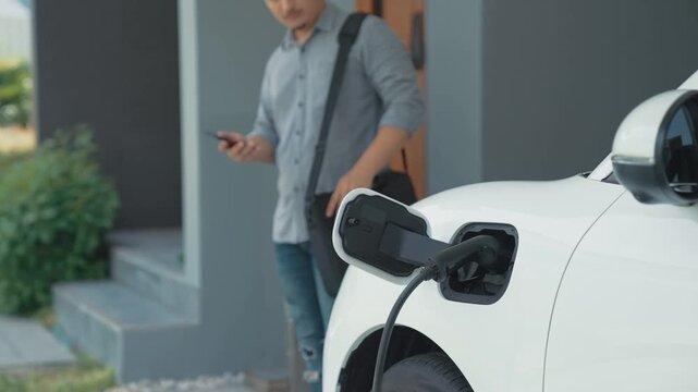 A man unplugs the electric vehicle's charger at his residence. Concept of the use of electric vehicles in a progressive lifestyle contributes to a clean and healthy environment.