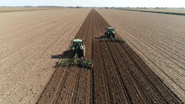 Tractors plowing and preparing farmland soil in parallel rows for large-scale agricultural planting