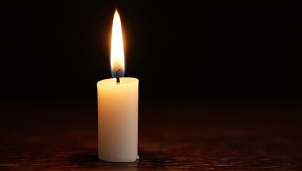 Single candle flame glowing in the dark on a wooden surface