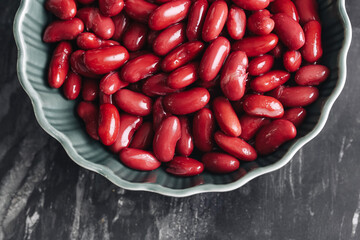 Red kidney beans in ceramic bowl. Healthy organic legumes rich in protein and fiber. Fresh raw beans on dark stone background. Natural vegetarian food and ingredient for cooking meals.