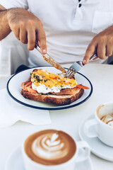 Man's hands cutting toast with salmon and eggs.