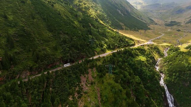 White bus rides by the highway in the beautiful green mountains. Drone footage over the narrow river flowing in the gulch. Romania nature.