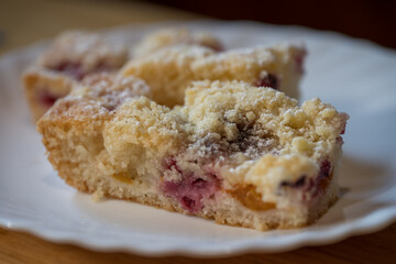 Homemade fruit cake sprinkled with sugar on a white plate on a wooden table.
