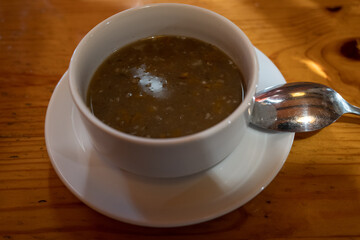 Lentil soup in a cup with a saucer on a wooden table.
