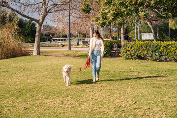 Young woman walking Golden Retriever dog in the park on a sunny day