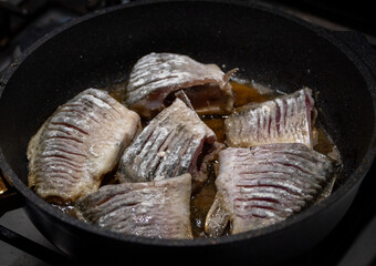 Fried crucian fish in a frying pan top view, close-up. Pieces of large fish in batter are fried in a frying pan in oil. Cooking fish in the home kitchen, deep fried fishes high-calorie food. 