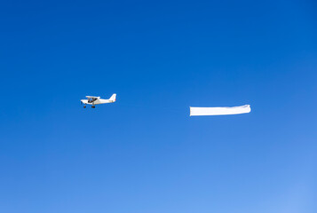 Small propeller airplane against clear blue sky flying with a clear white banner. © schab