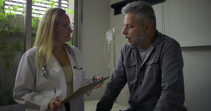 Female doctor gently delivering bad news to middle-aged male patient during serious medical consultation in clinic exam room - Powered by Adobe