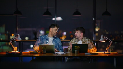 Skilful designers working late giving high five at evening office. Men rejoicing