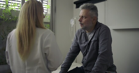 Female doctor delivering serious news to worried middle-aged male patient in clinical setting,...