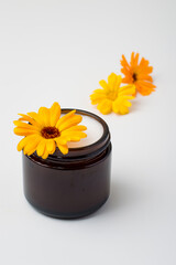 Jar of cream with calendula flower on light background. Beauty care, natural, plant cosmetics.