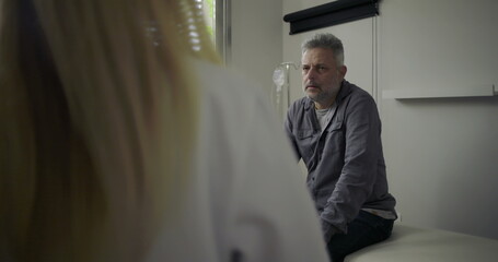 Female doctor delivering serious news to worried middle-aged male patient in clinical setting,...