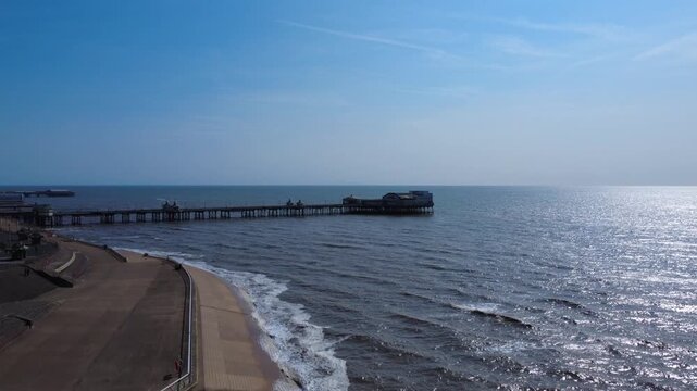Aerial climbing drone view of blackpool of Blackpool North Pier in late afternoon in summer with waves breaking on the promenade at high tide