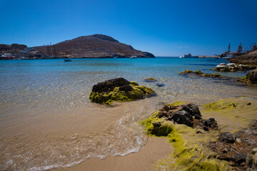 Fototapeta premium Morski pejzaż z kamienistą linią brzegową i odległymi górami pod czystym niebieskim niebem, Grecja, greckie wyspy