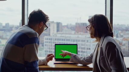 Two employees working chroma key device pointing screen in glass walls office