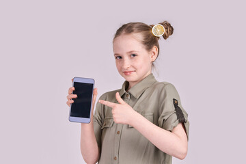 Caucasian young female child pointing at smartphone with lemon hair accessory on purple background.