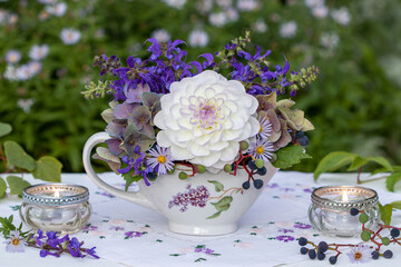 Blumen-Arrangement mit weißer Dahlie, Wiesensalbei und lila Hortensienblüten in einer Sauciere und Windlichtern	
