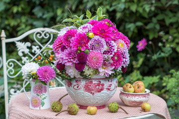 Blumen-Arrangement mit pink Dahlien in Pflanzvase, Äpfeln und Kastanien im Garten	
